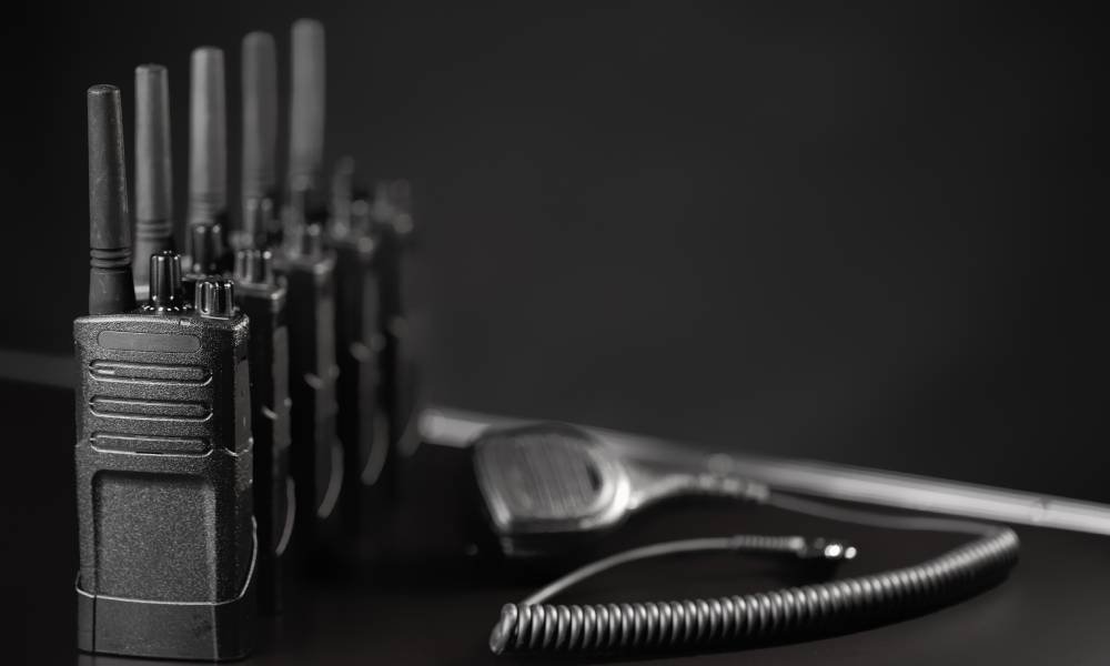 A set of five two-way radios lined up next to an unplugged microphone accessory against a black background.