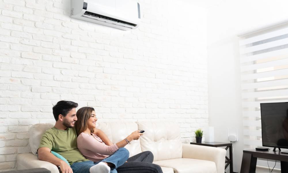 Young couple watches television set while enjoying the climate control offered by the mini split above their heads.